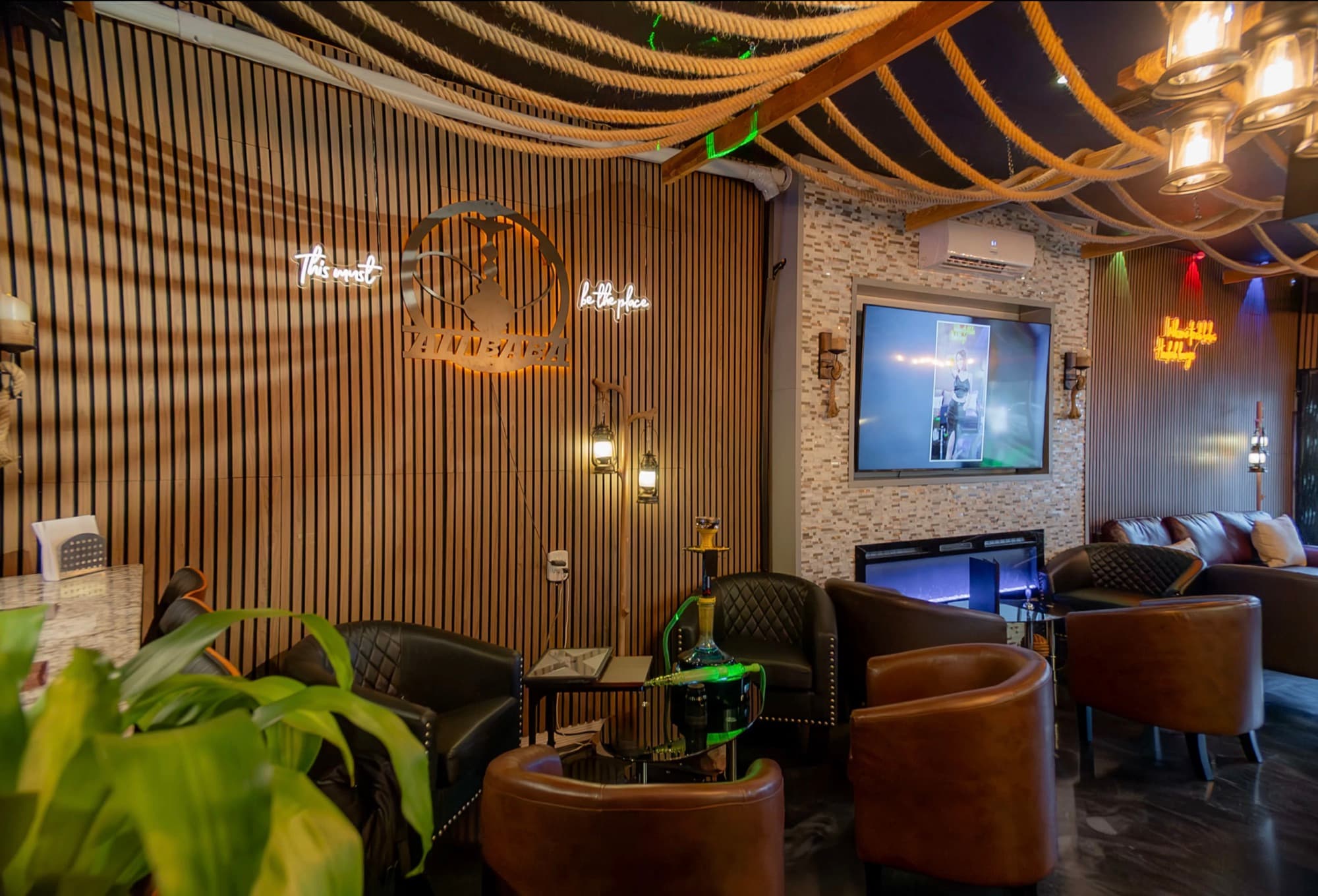 Leather armchairs and a hookah beside a wood-slat wall with a lit sign