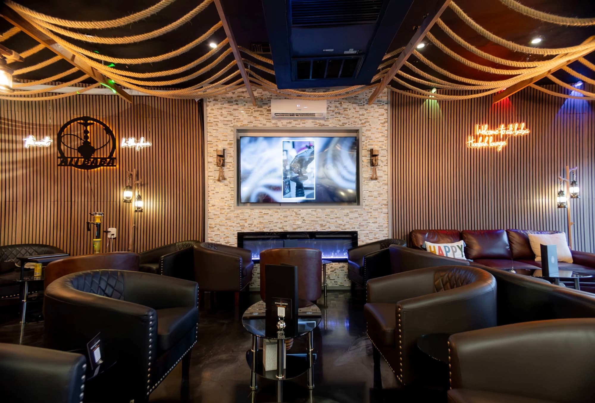 Wall TV above an electric fireplace between wood-slat walls with neon signs