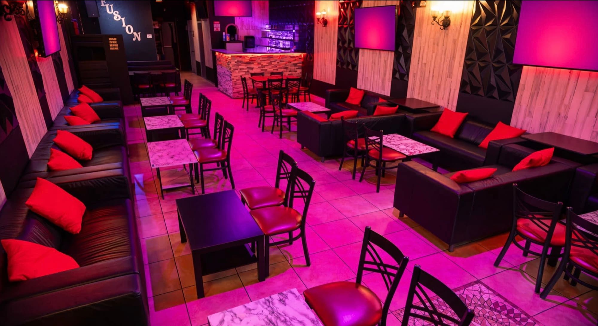 Pink-lit lounge with leather sofas, tables and the backlit bar in the distance